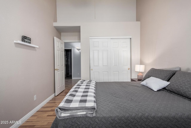 bedroom featuring a closet, wood finished floors, a towering ceiling, and baseboards