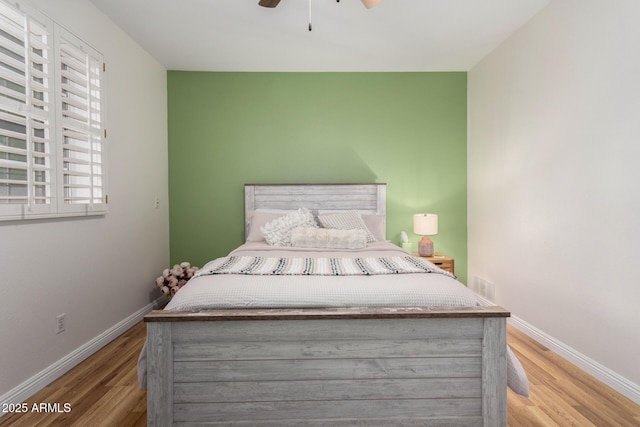 bedroom featuring visible vents, baseboards, ceiling fan, and wood finished floors