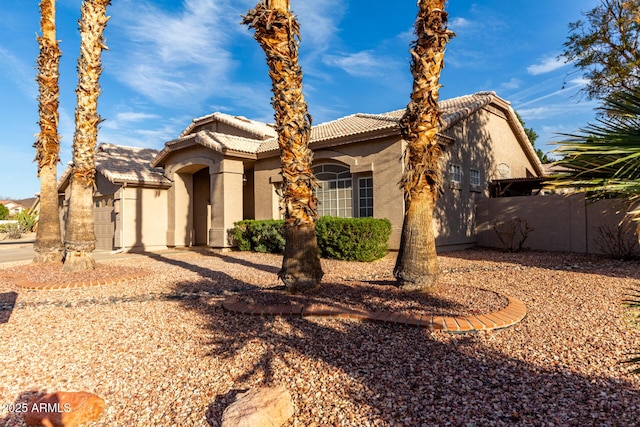 mediterranean / spanish home featuring fence, a tiled roof, and stucco siding