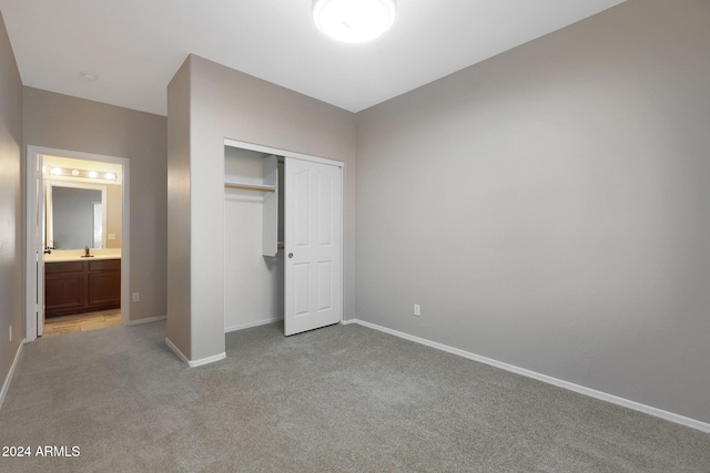 unfurnished bedroom with ensuite bathroom, a closet, light carpet, and sink