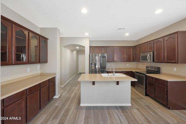 kitchen with a kitchen bar, appliances with stainless steel finishes, dark brown cabinets, sink, and light hardwood / wood-style flooring