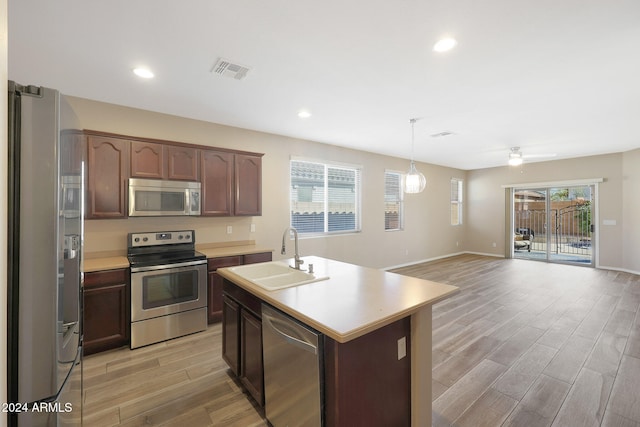 kitchen featuring appliances with stainless steel finishes, light wood-type flooring, sink, a center island with sink, and decorative light fixtures