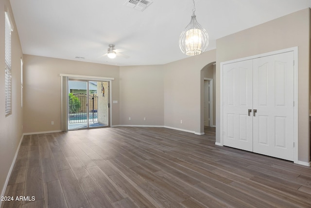 unfurnished room with ceiling fan with notable chandelier and dark hardwood / wood-style flooring