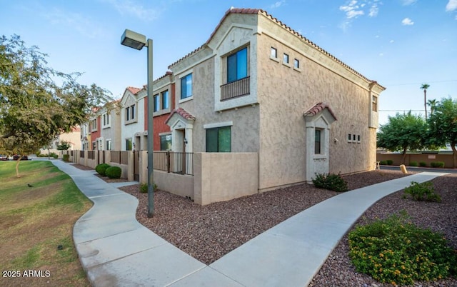 view of side of property with a tiled roof, fence, and stucco siding