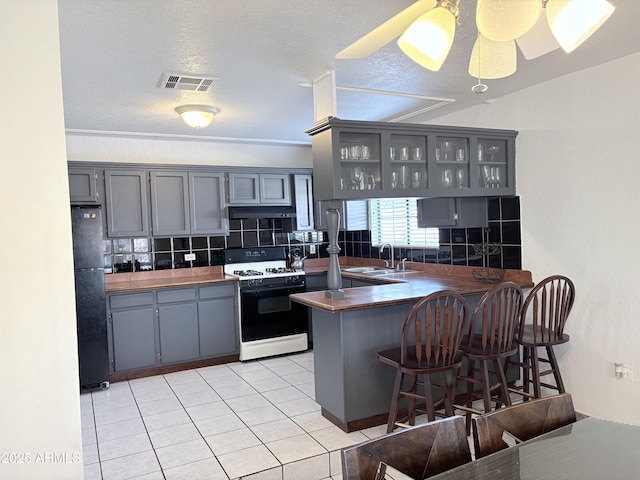 kitchen featuring gas stove, visible vents, freestanding refrigerator, gray cabinetry, and a sink