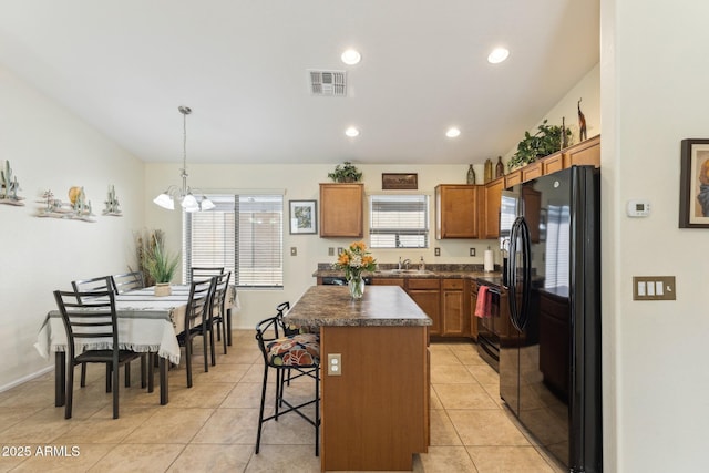 kitchen with light tile patterned floors, a kitchen island, visible vents, black appliances, and dark countertops