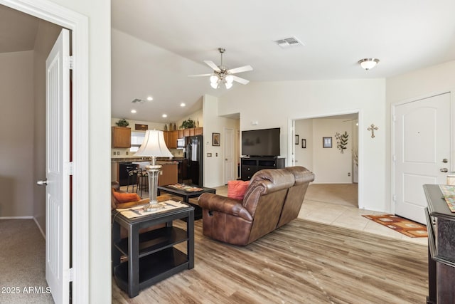 living room featuring light wood-style flooring, visible vents, vaulted ceiling, and a ceiling fan