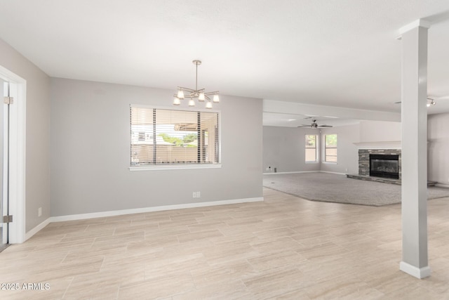 unfurnished living room featuring a fireplace, ceiling fan with notable chandelier, and baseboards