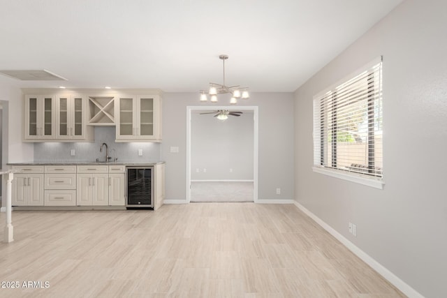 kitchen with beverage cooler, glass insert cabinets, decorative backsplash, a sink, and baseboards