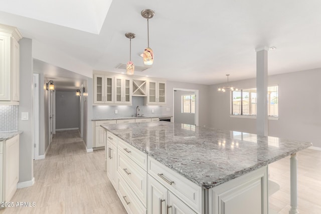 kitchen with white cabinetry, glass insert cabinets, a sink, a center island, and backsplash