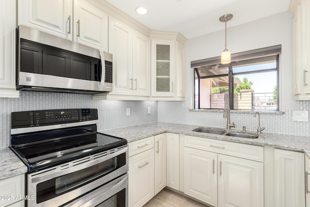 kitchen featuring stainless steel appliances, glass insert cabinets, light stone counters, backsplash, and hanging light fixtures