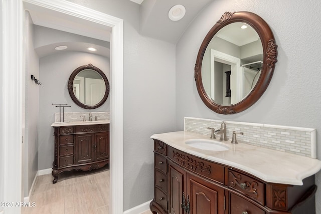 bathroom featuring baseboards, two vanities, decorative backsplash, and a sink
