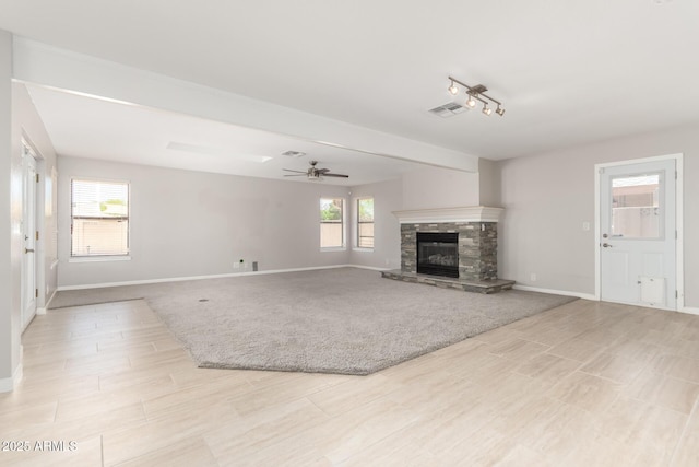 unfurnished living room featuring light wood-style flooring, a stone fireplace, baseboards, visible vents, and a ceiling fan