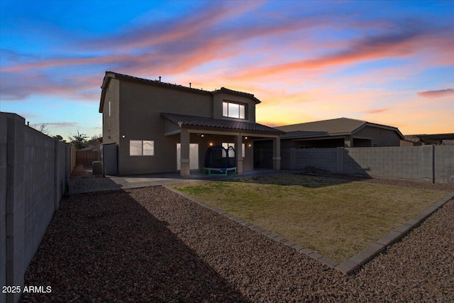 back house at dusk with a lawn and a patio area