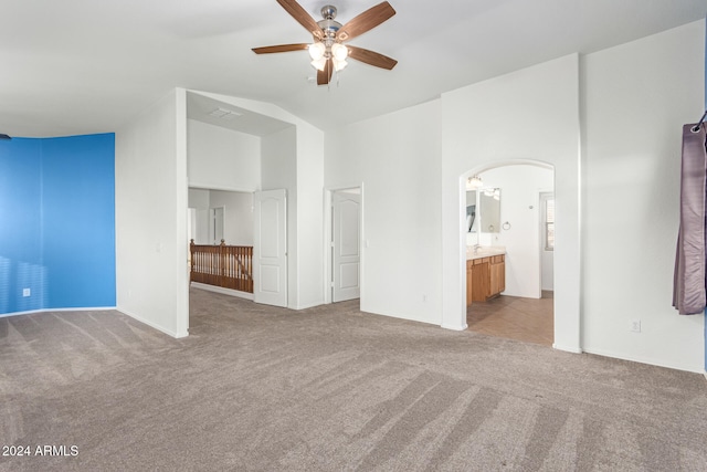 unfurnished bedroom featuring high vaulted ceiling, light colored carpet, ceiling fan, and ensuite bath