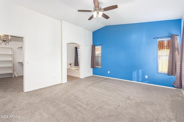 unfurnished bedroom featuring ceiling fan with notable chandelier, light colored carpet, vaulted ceiling, connected bathroom, and a spacious closet