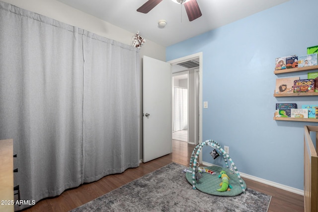 recreation room featuring a ceiling fan, baseboards, and dark wood-style flooring