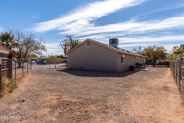 view of side of home featuring fence, central AC, and stucco siding