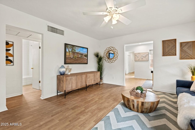 living room featuring visible vents, light wood-style flooring, a ceiling fan, baseboards, and attic access