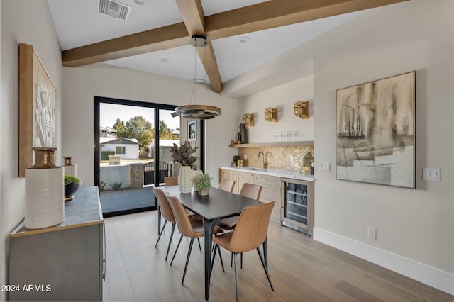 dining area featuring beamed ceiling, light hardwood / wood-style flooring, wet bar, and beverage cooler