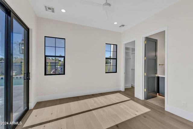 unfurnished bedroom with multiple windows, a spacious closet, a closet, and light hardwood / wood-style floors