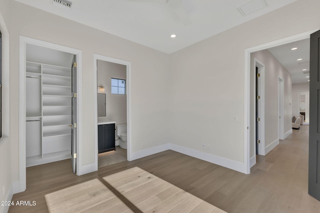 unfurnished bedroom with light hardwood / wood-style floors, a walk in closet, a closet, and ensuite bath