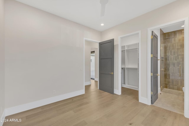 unfurnished bedroom with ensuite bathroom, a closet, a walk in closet, and light hardwood / wood-style flooring