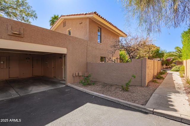 view of side of home with driveway, a tile roof, an attached garage, fence private yard, and stucco siding