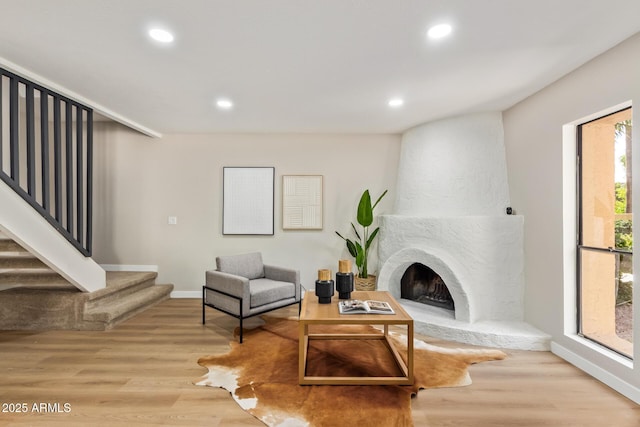 living area featuring a large fireplace, baseboards, stairway, wood finished floors, and recessed lighting