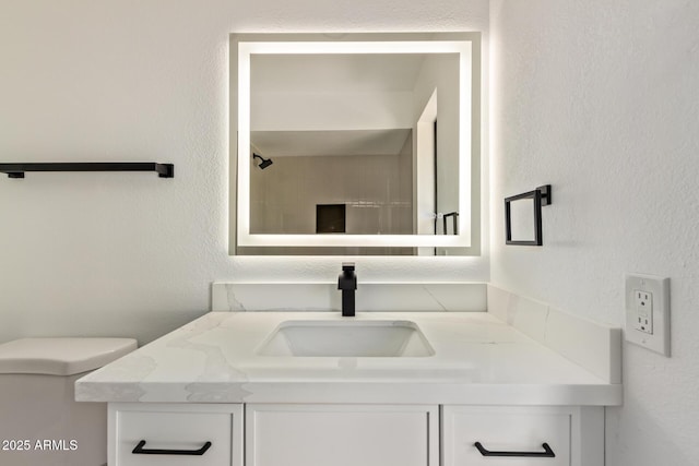 bathroom featuring toilet, a textured wall, and vanity