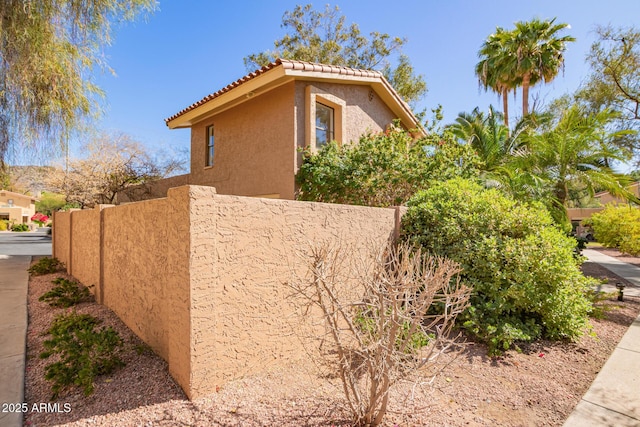 view of side of property with a tile roof, fence, and stucco siding