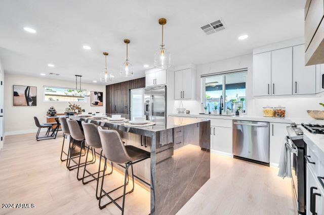 kitchen with a kitchen island, appliances with stainless steel finishes, white cabinetry, light wood-type flooring, and decorative light fixtures