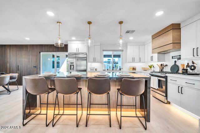 kitchen with appliances with stainless steel finishes, white cabinetry, custom range hood, and a kitchen island