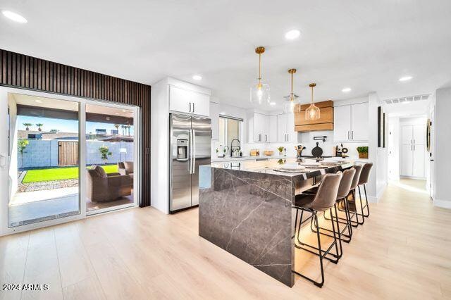 kitchen with stainless steel fridge, white cabinetry, decorative light fixtures, and light wood-type flooring