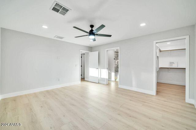 unfurnished bedroom with light hardwood / wood-style floors, a walk in closet, and ceiling fan