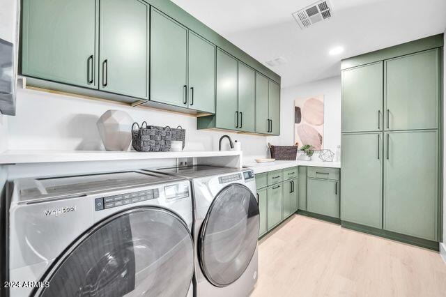 washroom featuring cabinets, light hardwood / wood-style flooring, and washer and clothes dryer