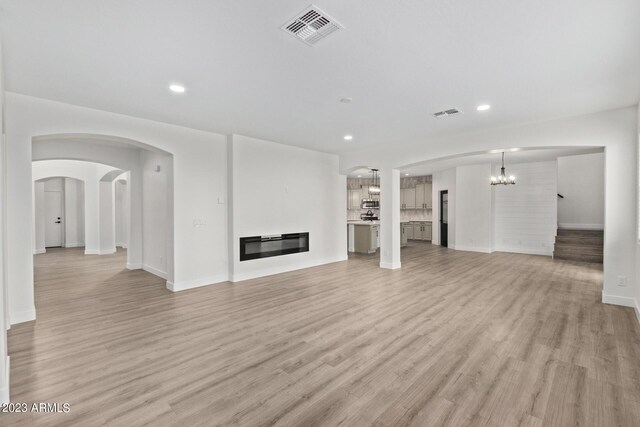 unfurnished living room with a notable chandelier and light wood-type flooring