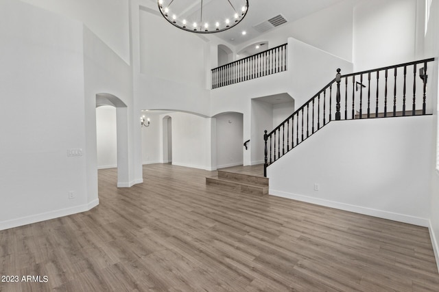 unfurnished living room featuring a high ceiling, light hardwood / wood-style floors, and a notable chandelier