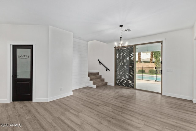 unfurnished room featuring a notable chandelier and light wood-type flooring