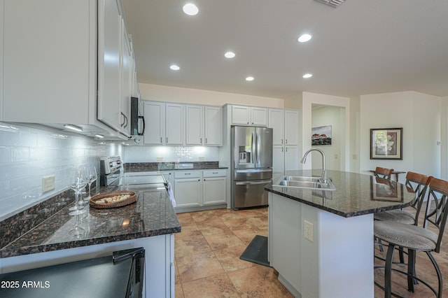 kitchen featuring dark stone countertops, decorative backsplash, a sink, stainless steel appliances, and a kitchen bar