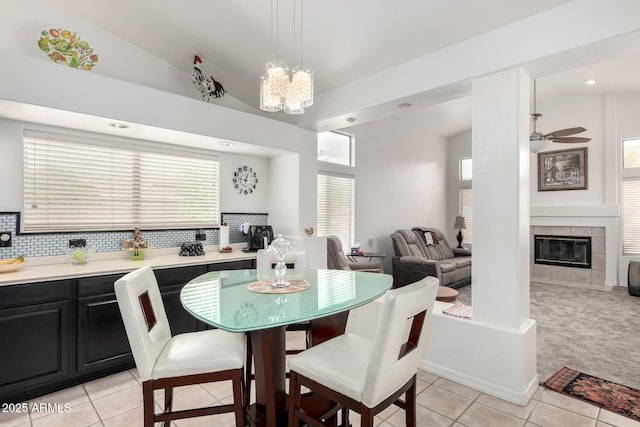 dining space featuring light tile patterned flooring, lofted ceiling, a tile fireplace, and light carpet