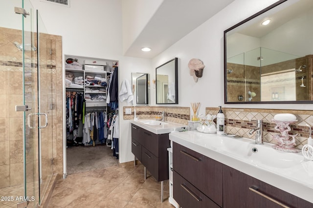 bathroom with decorative backsplash, a sink, a spacious closet, and a shower stall
