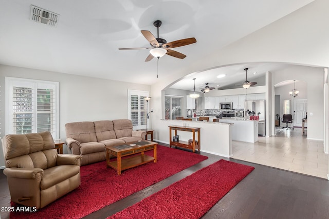 living room with vaulted ceiling, ceiling fan with notable chandelier, and light hardwood / wood-style flooring