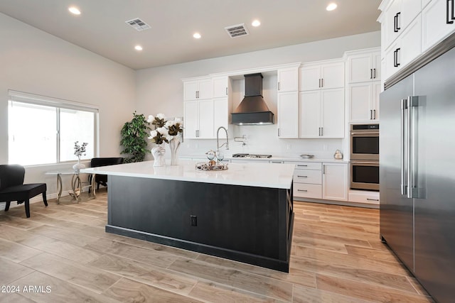 kitchen featuring stainless steel appliances, premium range hood, a kitchen island with sink, and white cabinetry