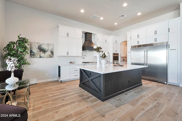 kitchen with light hardwood / wood-style floors, an island with sink, white cabinets, custom exhaust hood, and built in fridge