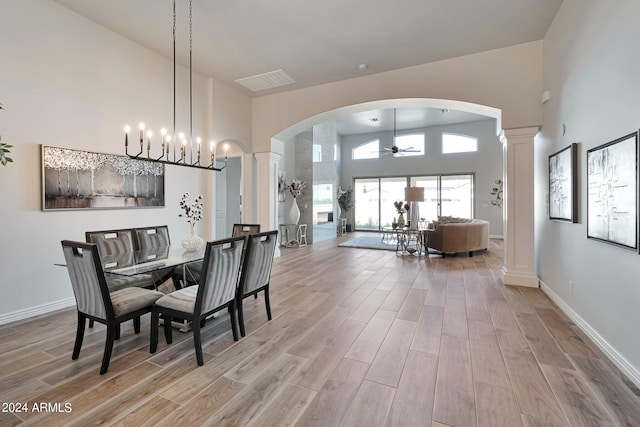 dining space with a high ceiling, decorative columns, ceiling fan, and light wood-type flooring