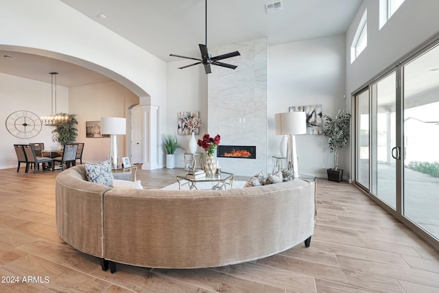 living room with a premium fireplace, a towering ceiling, ceiling fan with notable chandelier, and light hardwood / wood-style flooring