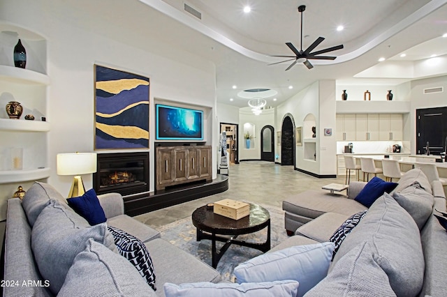 living room with built in shelves, a raised ceiling, and ceiling fan