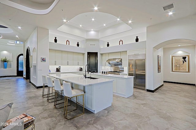 kitchen with a kitchen bar, a kitchen island with sink, sink, built in refrigerator, and white cabinetry