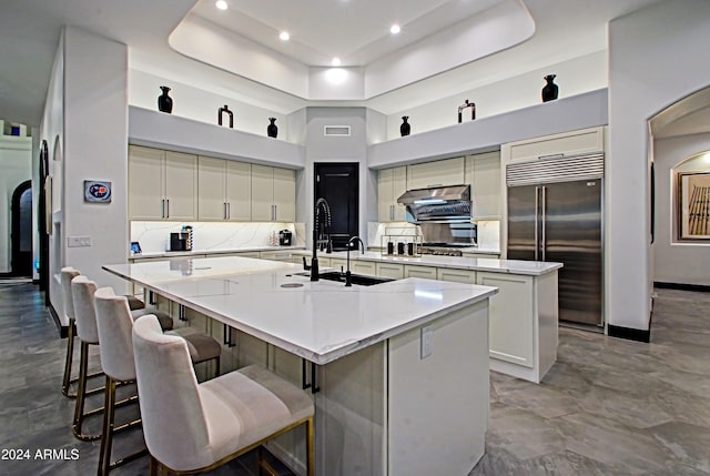 kitchen featuring decorative backsplash, a kitchen breakfast bar, a towering ceiling, stainless steel built in refrigerator, and a large island with sink